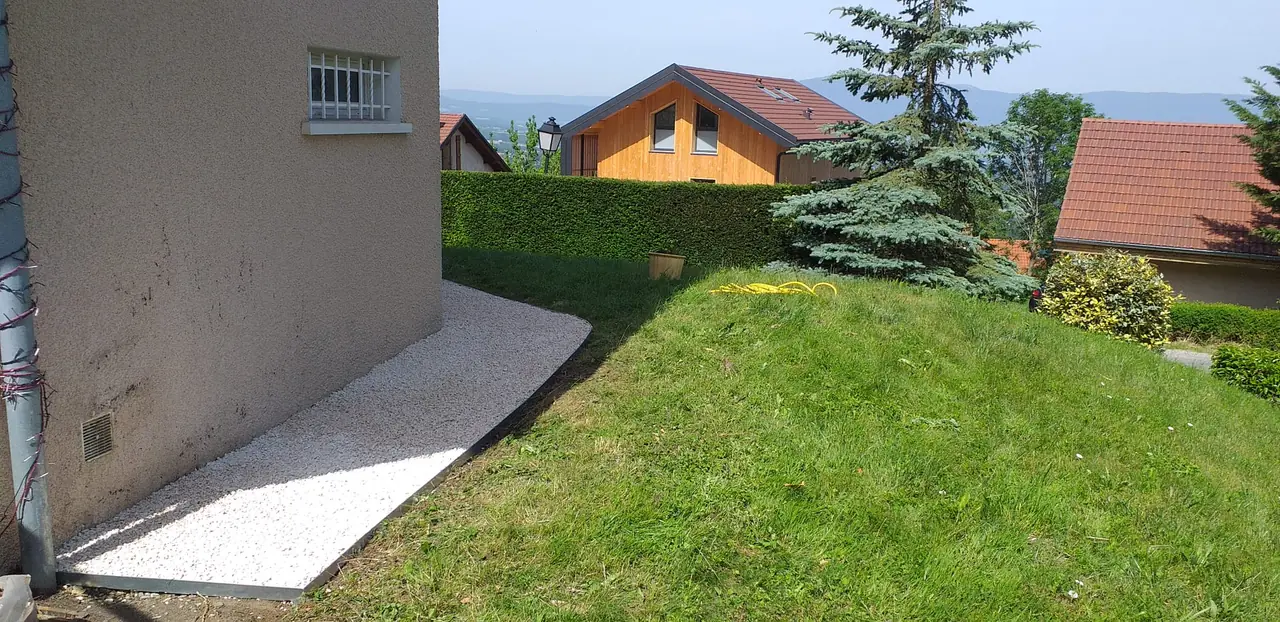 Bande de gravier posée en pied de façade, bordure droite côté herbe.